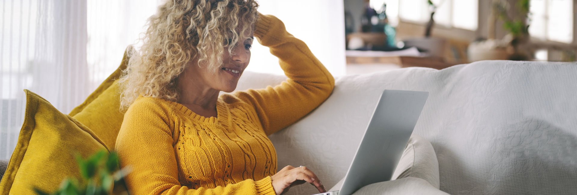 Woman-in-yellow-sweater-on-laptop-consolidating-her-debt-with-a-home-equity-loan-while-relaxing-on-couch.